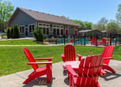 Thumbnail 25 of 49 - Outdoor seating area at the Retreat at Indian Lake apartments in hendersonville with four red Adirondack chairs around a matching table.