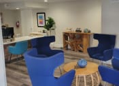 Thumbnail 52 of 60 - Fusion Orlando apartments reception desk and waiting area with four modern navy blue chairs around a round wooden coffee table.