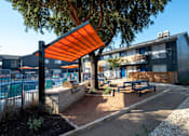 Thumbnail 20 of 36 - Poolside patio at Studio 700 apartments in Arlington, Texas with picnic table and grill with large prepping stations under an oak tree and large shade.
