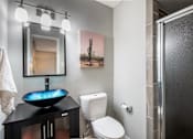 Thumbnail 14 of 36 - Modern bathroom in Stadium 700 one bedroom apartments in Arlington, TX with a luxury basin sink, toilet, and shower with frosted glass door.