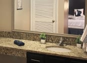 Thumbnail 23 of 60 - Fusion Orlando studio apartment kitchen bathroom vanity with long granite inspired countertop, double mirror, and single sink.