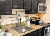 Thumbnail 19 of 60 - Fusion Orlando efficiency studio apartments in Orlando, Florida kitchen with espresso cabinets, electric stove, stainless steel microwave, and white subway tile backsplash.
