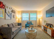 Thumbnail 1 of 25 - Living room in the Canvas East Nashville Apartments with midcentury modern decor, large couch, and double wide windows with blinds and curtains.