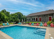 Thumbnail 20 of 36 - Retreat at Indian Lake Apartments Hendersonville TN swimming pool with red chairs and a building in the background.