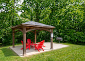Thumbnail 31 of 36 - A wooden gazebo at The Retreat at Indian Lake Apartments in Hendersonville TN with red chairs is surrounded by greenery.