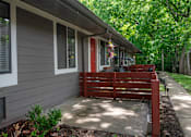 Thumbnail 30 of 36 - A grey apartment at The Retreat Apartments with a red door and a red bench outside.