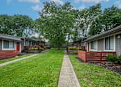 Thumbnail 28 of 36 - A row of studio and one bedroom apartments at The Retreat at Indian Lake with green lawns and trees in the background.