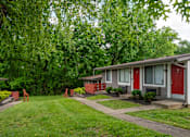Thumbnail 25 of 36 - A row of studio and 1 bedroom apartments at The Retreat Apartments in Hendersonville with red doors and green trees in the background.
