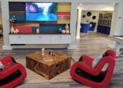 Thumbnail 56 of 60 - Fusion Orlando apartments lounge television on colorful pallet wall and two red modern rocking chairs around a wooden block coffee table.