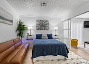 Thumbnail 12 of 41 - A bedroom with a blue bedspread and a brown leather couch.