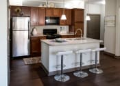 Thumbnail 1 of 25 - A modern kitchen at Austin Park Apartments in Miamisburg, Ohio features dark brown cabinets, granite-style countertops, an island with barstools, and stainless steel appliances.