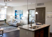 Thumbnail 2 of 25 - The living room in this updated modern interior at Austin Park Apartments in Miamisburg, Ohio showcases hardwood flooring, granite-style countertops, and a kitchen island, welcoming pets.