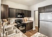Thumbnail 1 of 28 - A kitchen equipped with stainless steel and black appliances, granite countertops, dark wood cabinets, and hardwood-style flooring.