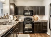 Thumbnail 12 of 28 - The Fort kitchen equipped with granite countertops, black appliances, and hardwood-style flooring.
