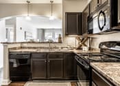 Thumbnail 10 of 28 - A kitchen at The Fort equipped with dark wood cabinets, black appliances, light fixtures, and hardwood-style flooring.