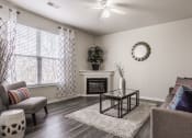 Thumbnail 3 of 29 - Eagle Creek, IN Apartments For Rent - Riverchase - Living Room With Hardwood Floors, A Ceiling Fan, A Decorative Fireplace, And A Window With Blinds
