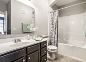 Thumbnail 15 of 28 - A bathroom with a large vanity and a mirror, and a white tub with white tile walls.