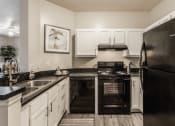 Thumbnail 13 of 29 - Eagle Creek, IN Apartments - Riverchase - Kitchen With White Cabinets, Hardwood Flooring, Dual Sinks, And Black Appliances