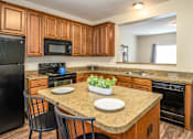 Thumbnail 23 of 55 - Pet Friendly Apartments in Pickerington, OH - Arbors at Turnberry - Kitchen with Wood-Style Cabinetry, Black Appliances, Granite-Style Counters, Overhead Lighting, as well as an Island with Seating