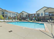Thumbnail 13 of 25 - The pool area at Austin Park Apartments offers lounge chairs, a comfortable couch, and tables for residents to enjoy.