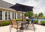 Thumbnail 15 of 27 - Apartments for Rent in Hilliard, OH - Residences at Breckenridge - BBQ Area Near the Pool with a Grill, a Table, Chairs, and an Umbrella