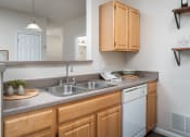 Thumbnail 3 of 21 - Kitchen at Catalina Club in Pataskala, OH, featuring wood-style cabinetry, grey countertops, a breakfast bar, and a white dishwasher.