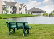 Thumbnail 19 of 21 - Peaceful pond at Catalina Club Apartments in Pataskala, OH, surrounded by green grass and featuring a bench for enjoying the view.