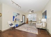 Thumbnail 6 of 25 - The living room in a one-bedroom apartment features wood-inspired flooring, a ceiling fan, modern light fixtures, and a large window with blinds.