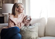 Thumbnail 36 of 55 - A woman in a pink sweater is sitting on a couch holding a mug.