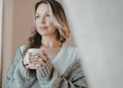 Thumbnail 37 of 55 - A woman in a grey sweater is holding a white mug.