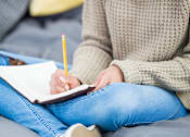 Thumbnail 46 of 55 - A person is writing in a notebook with a yellow pencil.