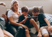 Thumbnail 54 of 55 - A family of four is sitting on a couch, each using a tablet.