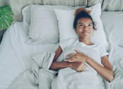 Thumbnail 55 of 55 - A woman is lying in bed with her hand on her chest.