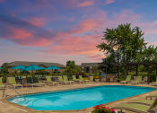 Thumbnail 4 of 25 - Resort-style swimming pool with lounge chairs and umbrellas, located beside a charming brick building at The Coleman in Canal Winchester, OH