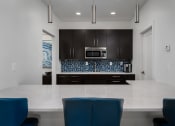 Thumbnail 10 of 25 - Contemporary kitchen with large island, white countertops, and blue bar stools at The Coleman Apartments