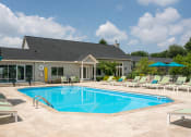 Thumbnail 20 of 25 - Swimming pool at The Coleman in Canal Winchester, OH, with chaise lounge chairs, sun umbrellas, and a modern gray building in the background
