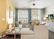 Thumbnail 2 of 11 - A living room with a beige sofa, a wooden coffee table, and a ceiling fan.
