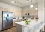 Thumbnail 6 of 14 - A modern kitchen with a large island and stainless steel appliances.
