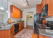 Thumbnail 11 of 24 - A kitchen with wooden cabinets and a black refrigerator.