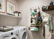 Thumbnail 17 of 34 - A laundry room with two washing machines and a shelf with hanging clothes.