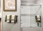Thumbnail 52 of 56 - A bathroom with a white tiled shower and a white bathtub.