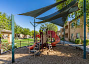 Thumbnail 3 of 24 - A playground with a red slide and a grey slide under a shade structure.