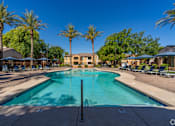 Thumbnail 6 of 24 - A large swimming pool surrounded by palm trees and lounge chairs.