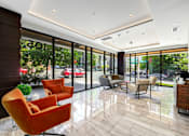 Thumbnail 20 of 38 - a lobby of a hotel with orange chairs and glass doors
