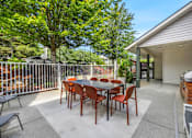 Thumbnail 15 of 34 - A patio with a table and chairs is surrounded by a fence and trees.