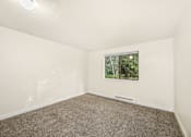 Thumbnail 12 of 26 - A room with a carpeted floor and a window showing trees outside.