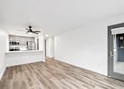 Thumbnail 4 of 13 - A room with a ceiling fan and a kitchen area in the background.
