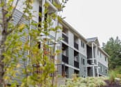 Thumbnail 19 of 24 - an apartment building with gray siding and green trees