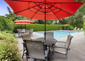Thumbnail 26 of 29 - a poolside patio with a table and chairs under a red umbrella