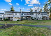 Thumbnail 33 of 41 - Apartment complex with a grassy area in front and trees in the background.